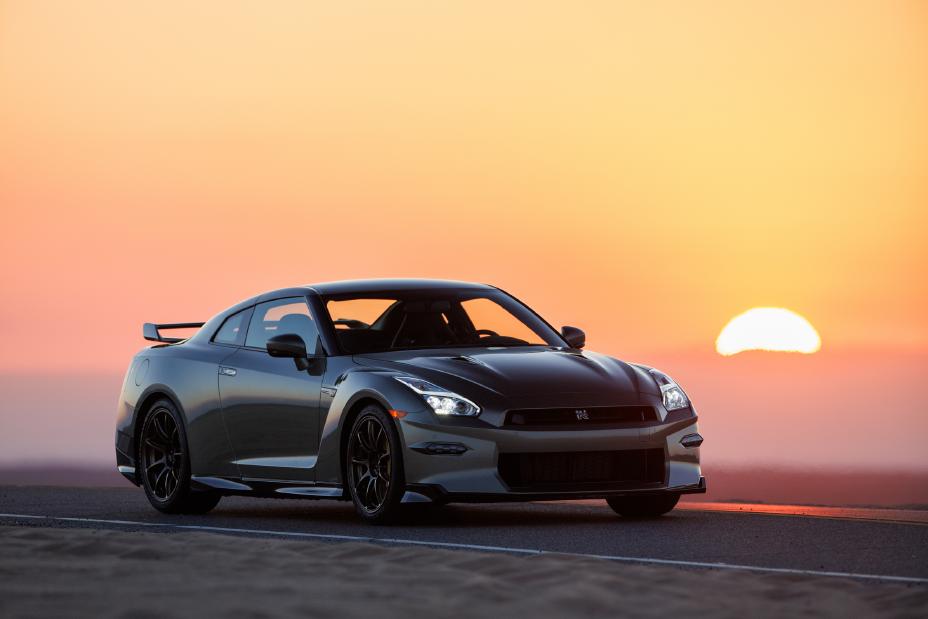 Front right ¾ angle of the 2024 Nissan GT-R driving along a desert highway with a vibrant sunset behind.