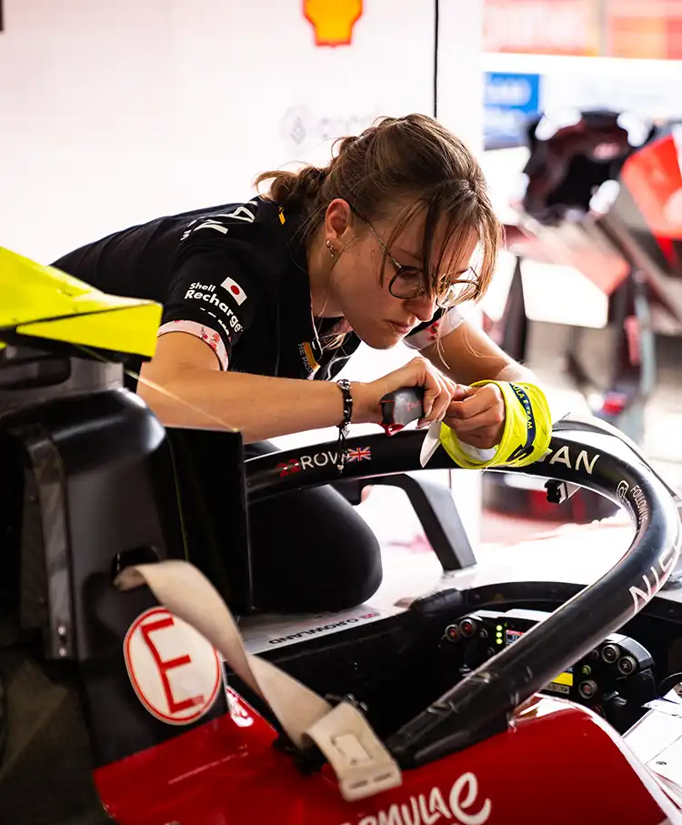 A woman in Nissan Formula E gear on a laptop near the race track.