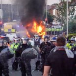 Article thumbnail: SOUTHPORT, ENGLAND - JULY 30: Riot police hold back protesters near a burning police vehicle after disorder broke out on July 30, 2024 in Southport, England. Rumours about the identity of the 17-year-old suspect in yesterday's deadly stabbing attack here have sparked a violent protest. According to authorities and media reports, the suspect was born in Cardiff to Rwandan parents, but the person cannot be named due to his age. A false report had circulated online that the suspect was a recent immigrant who crossed the English Channel last week and was "on an MI6 watchlist." (Photo by Getty Images/Getty Images)