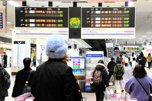 東武東上線・池袋駅の電光掲示板を眺める乗客たち。左側の掲示板には、韓国語が表示されている。言語は、日本語10秒→英語8秒→中国語4秒→ハングル4秒の周期で変わっていた=2025年2月20日午後4時7分、東京都豊島区西池袋、平川仁撮影