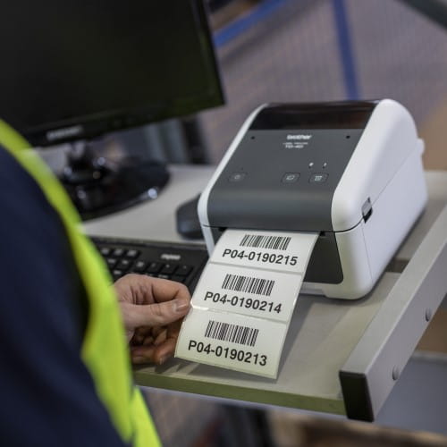 A man in a high visibility vest taking labels that have been printed by a Brother TD printer