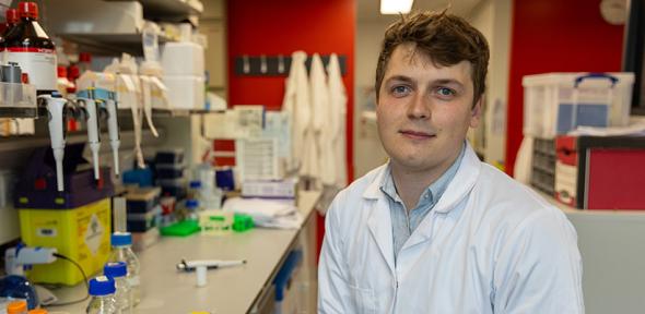 Cancer researcher Tom Else sitting in a lab wearing a white lab coat