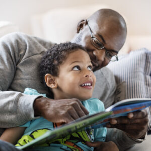 Smiling boy looking at father while reading picture book at home