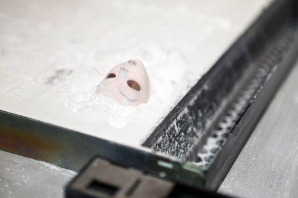 After the white powder is brushed and blown away, a color 3D printed face is revealed underneath.