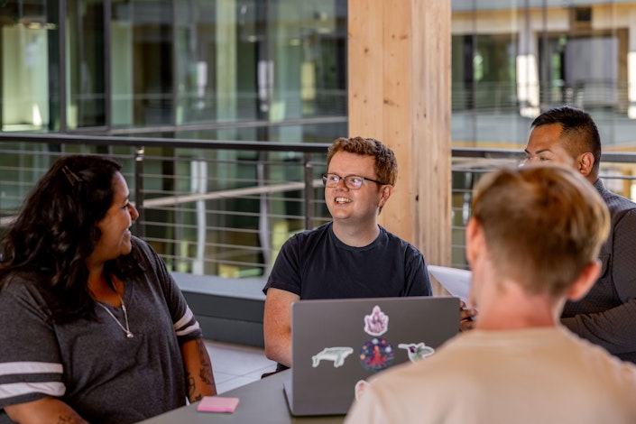 A group of Ai2 team members talking around a laptop at a table outdoors.