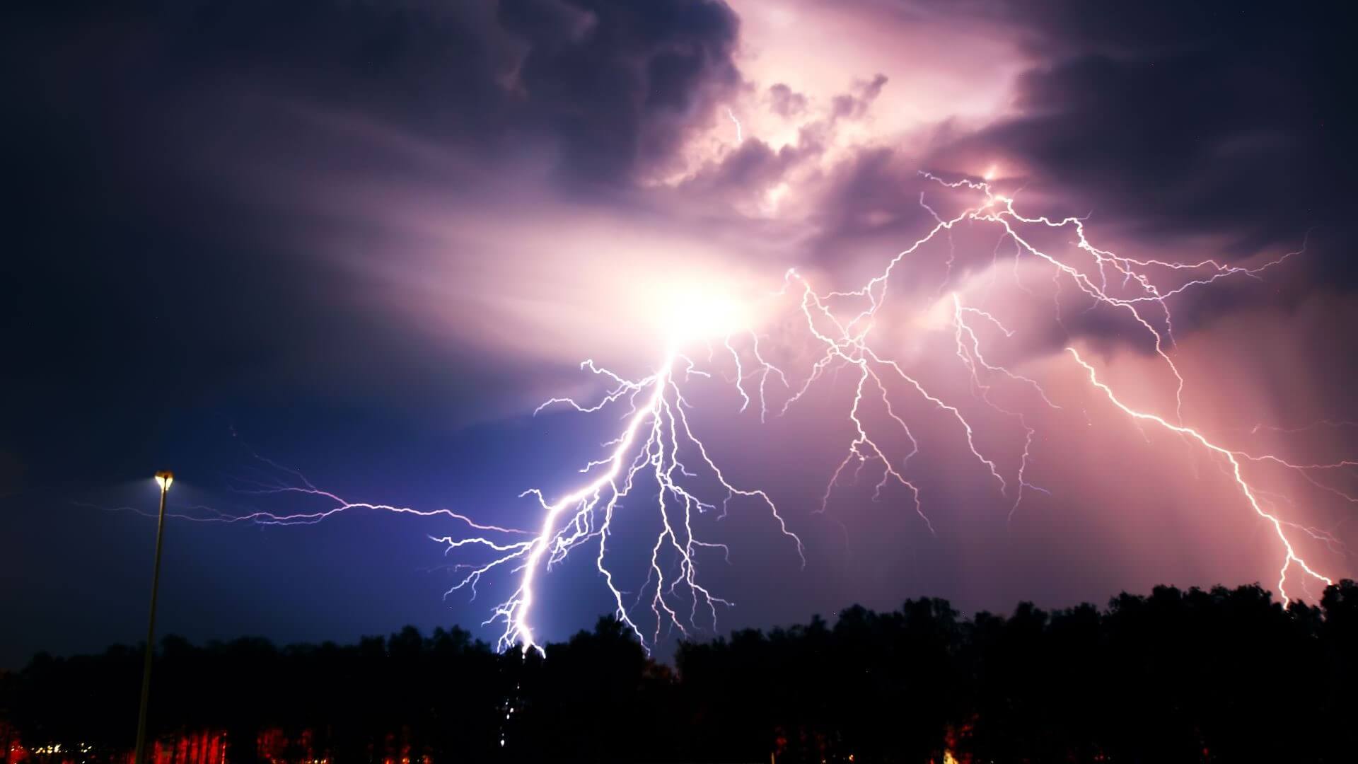 Bright flashes of lightning striking ground silhouetted against dark nightime sky and clouds