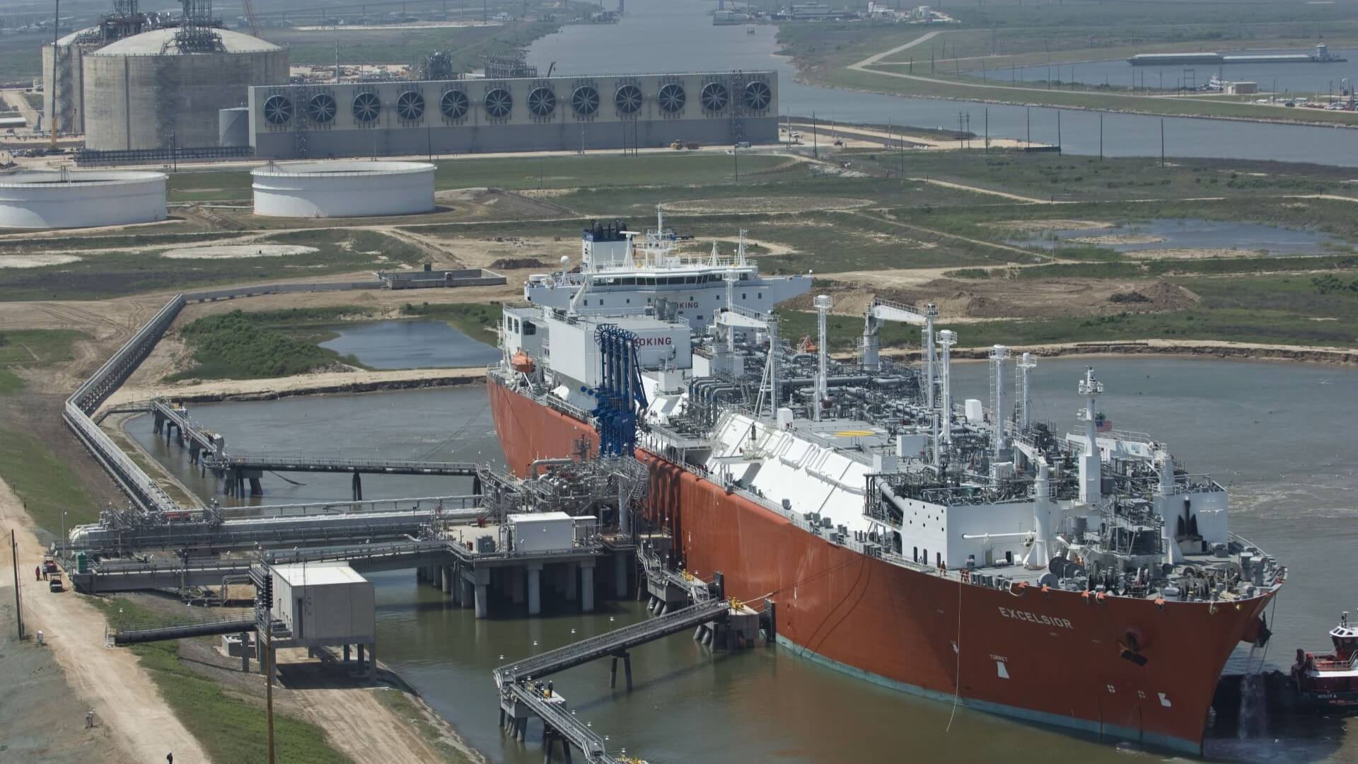 Aerial view of tanker refuelling at LNG terminal, with storage tanks in background