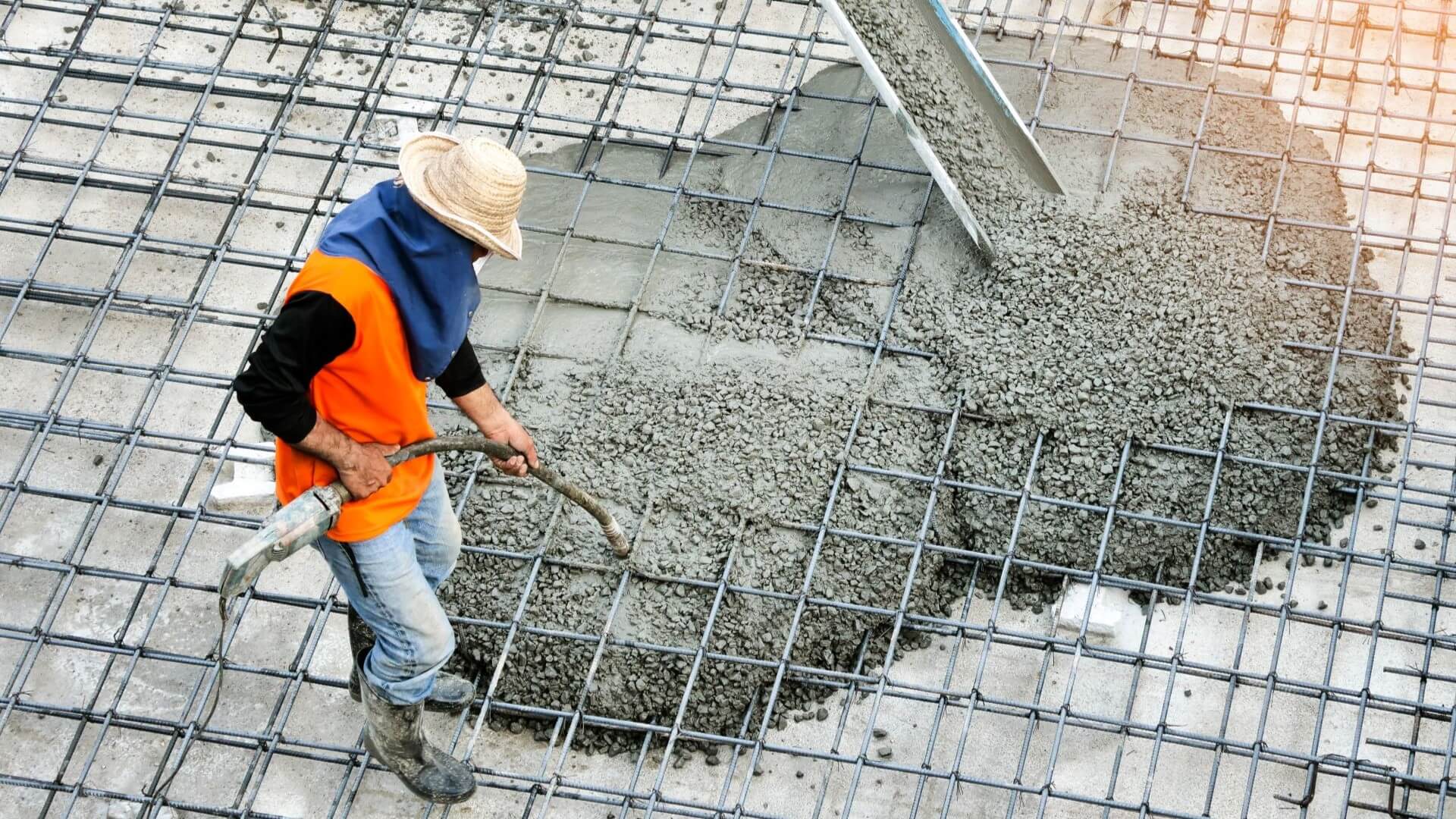 Overhead photo of man in hat and high-vis jacket spreading concrete on metal mesh