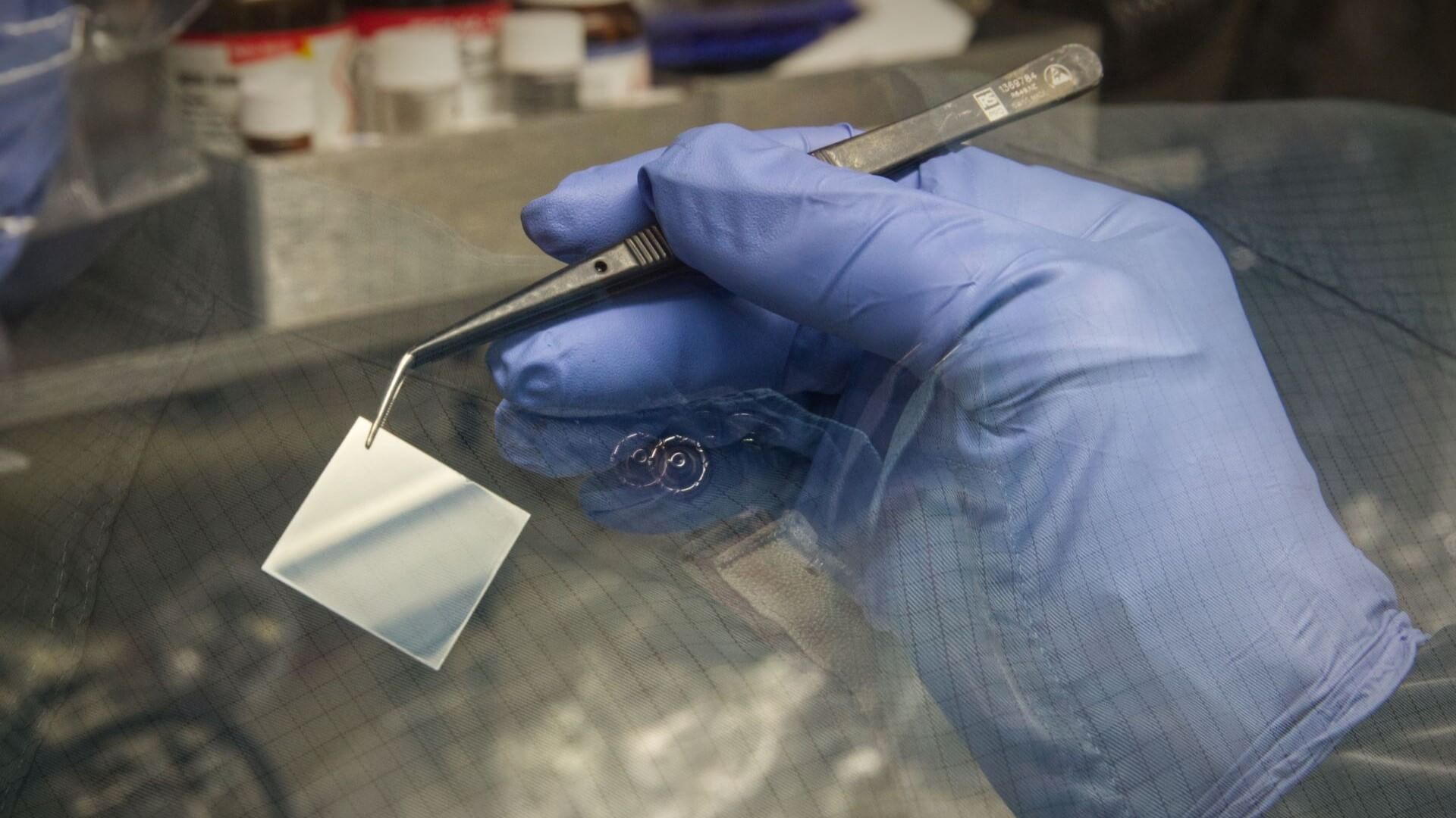 Gloved hand holding solar material with tweezers