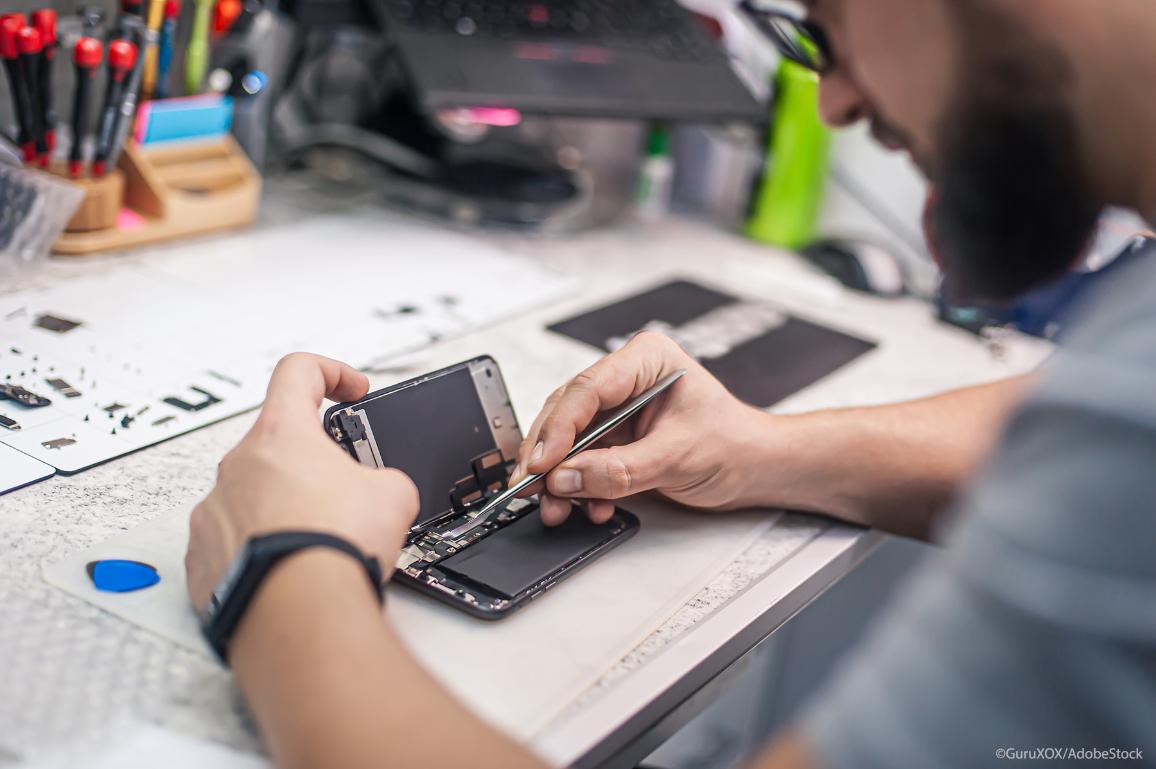 In an electronics repair shop, a repairman repairs a smartphone.
