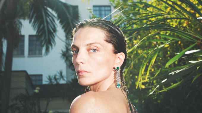 A woman wears a dangly earring in white gold with Paraíba tourmalines, emeralds and diamonds