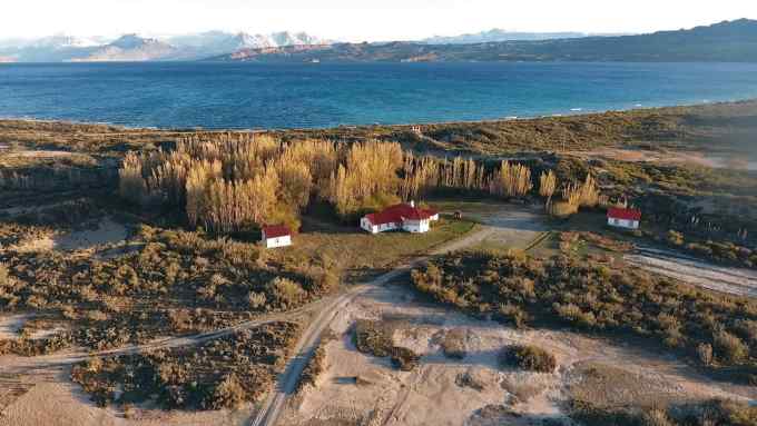 A view from above of several white building with red roofs. Behind them is a large blue lake and a snowcapped mountain