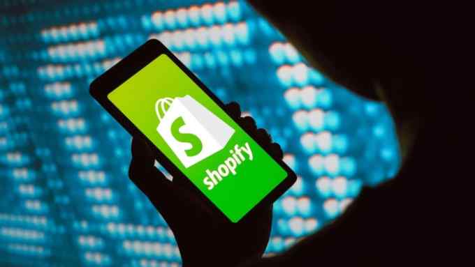 A person holding a smartphone. The Shopify logo appears in the smartphone screen