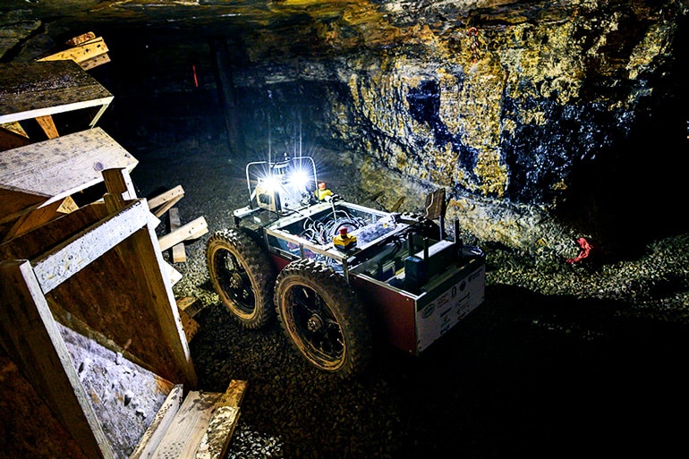 The robot moves through the dark test mine with its headlights on.