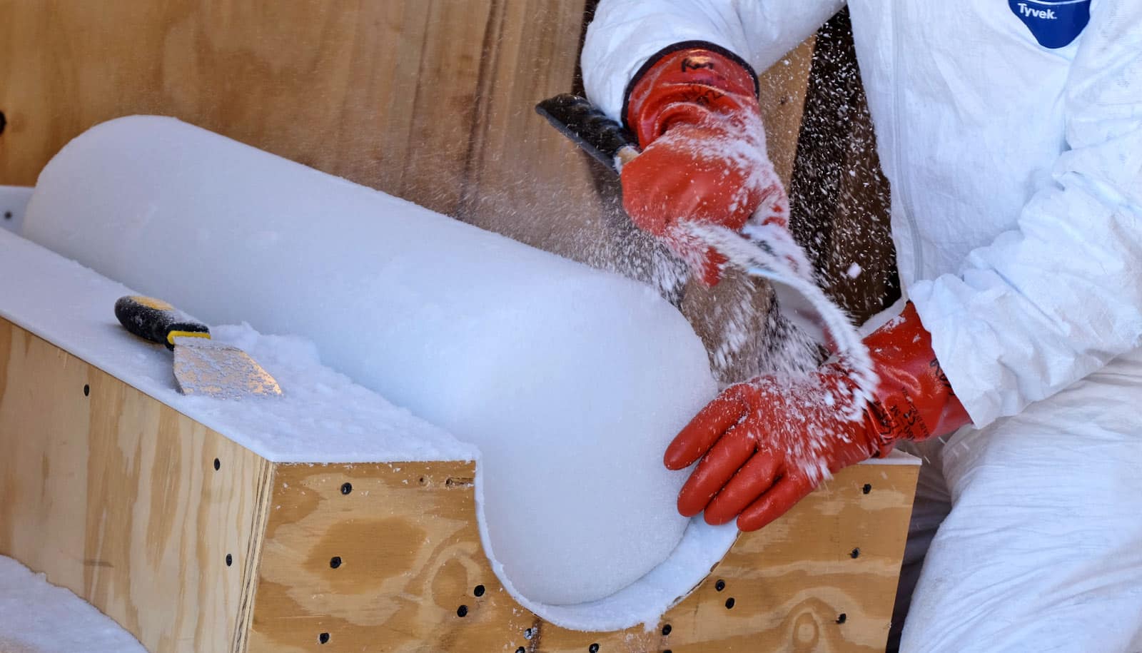 gloved hands use tool to scrape ice core in wooden holder