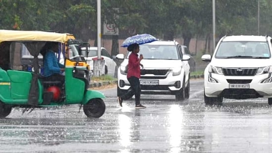 A woman with an umbrella crossing a busy road as rain lashed Chandigarh.  (Ravi Kumar/ HT)