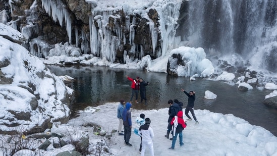 Tourists visit a partially frozen waterfall in Drang village, northwest of Srinagar. Kashmir has been going through a prolonged dry spell and a 79 per cent deficit in rainfall was recorded for December.(AP)