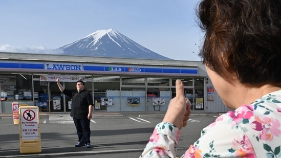 A person takes pictures of Mount Fuji from across the street of a Lawson convenience store, hours before the installation of a barrier to block the sight of Japan's Mount Fuji to deter badly behaved tourists.(AFP)