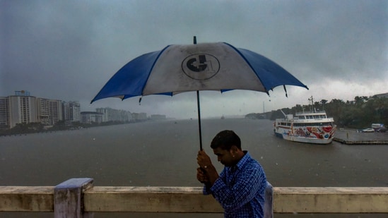 A man uses an umbrella in the rain on Wednesday, May 29, 2024, against the backdrop of Kochi's backwaters.(PTI)
