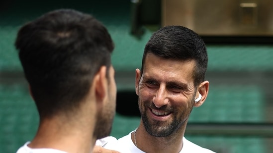 Serbia's Novak Djokovic smiles at Spain's Carlos Alcaraz during a warm up session on centre court at the All England Lawn Tennis Club, in west London on June 27, 2024, the week before the Wimbledon Championships(AFP)