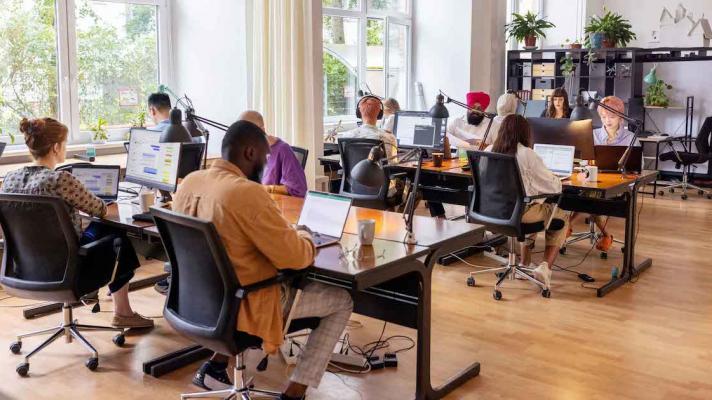 Numerous people sitting at large desks in a big room