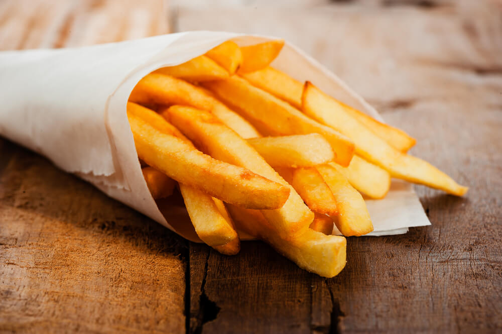 yummy homemade fries in a white paper bag on wooden table