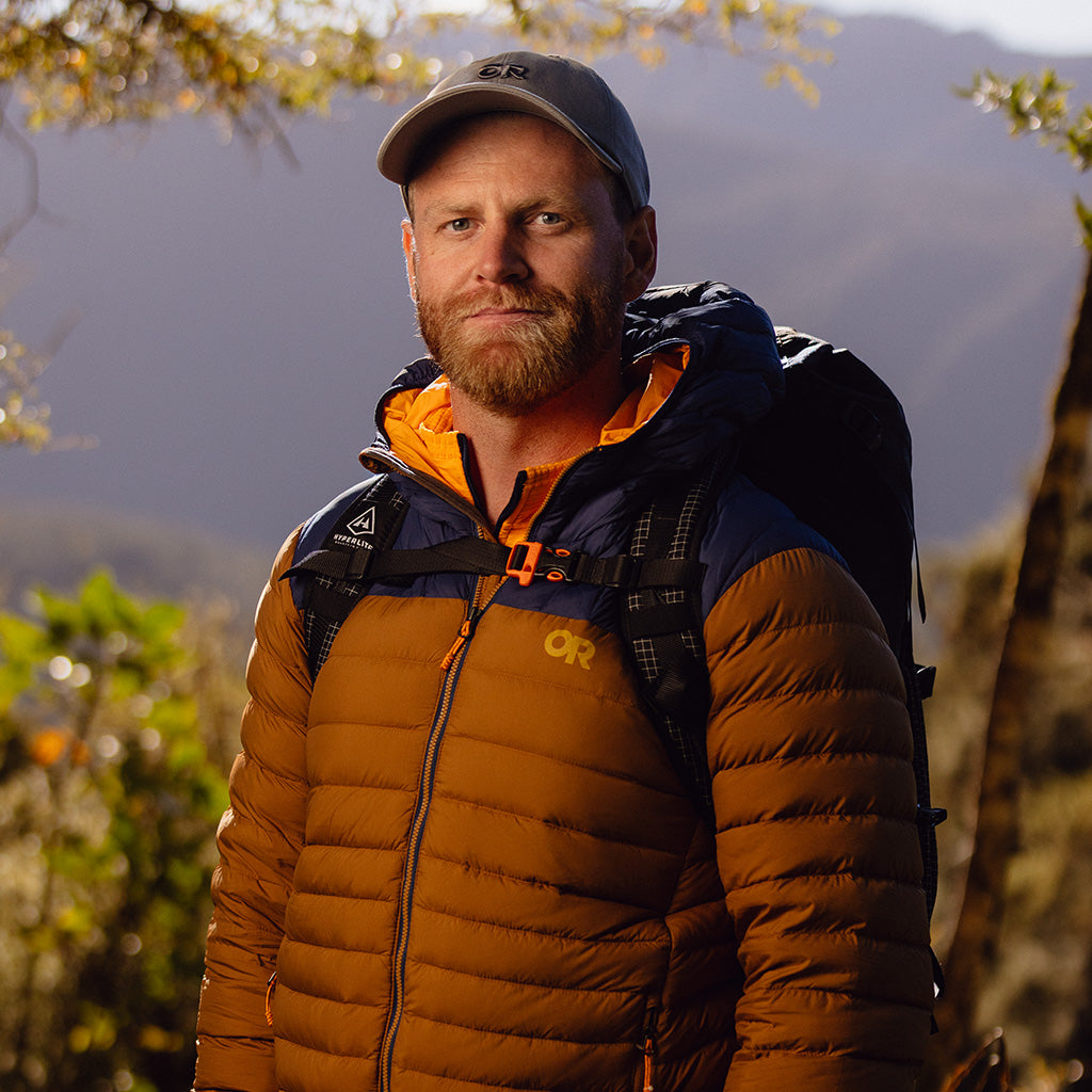 Man wears Outdoor Research Transcendent Down Hoodie in Bronze/Cenote during his hike.