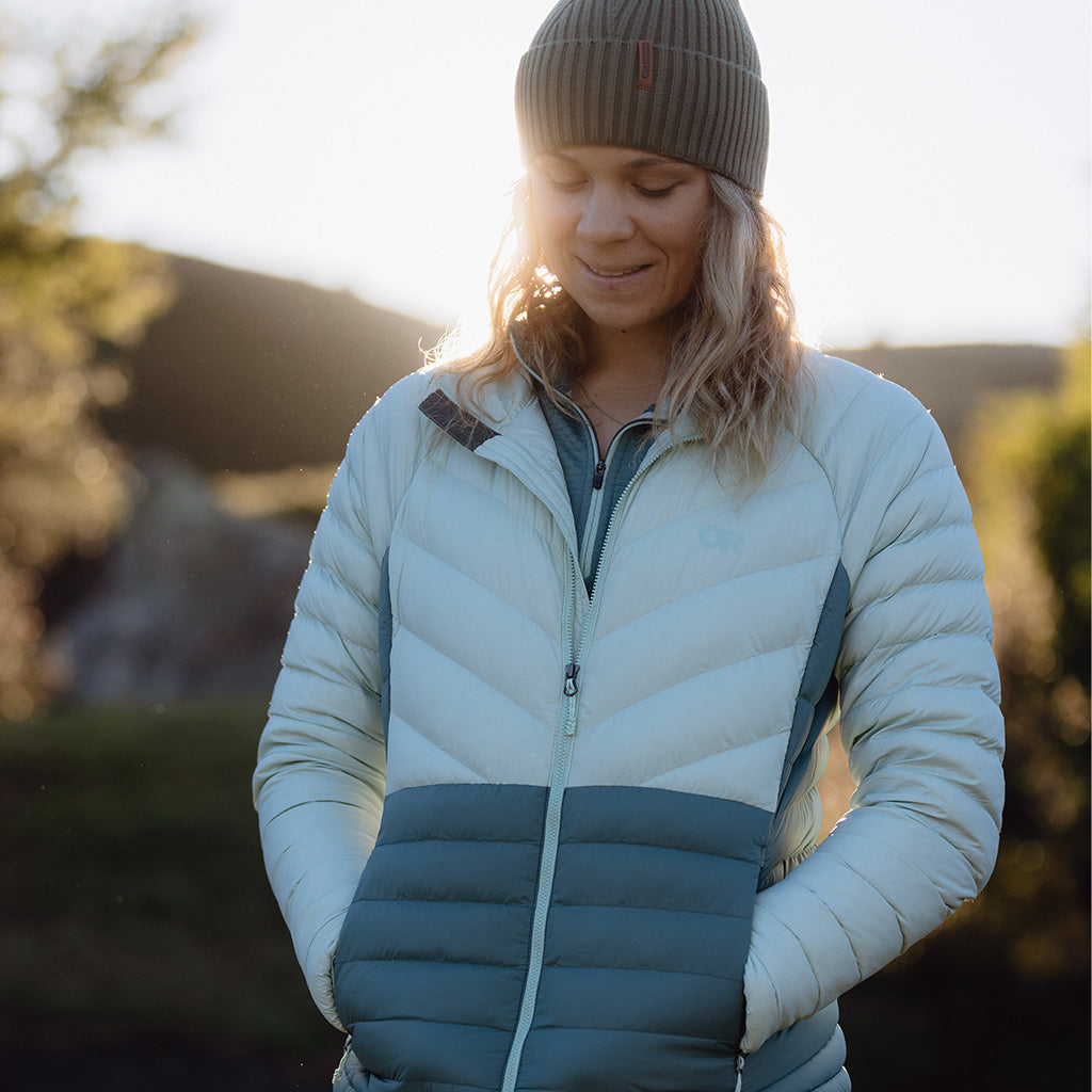 Woman smiles with her hands in the pockets of her Transcendent Down Jacket in Fresh Mint/Neptune blue. 