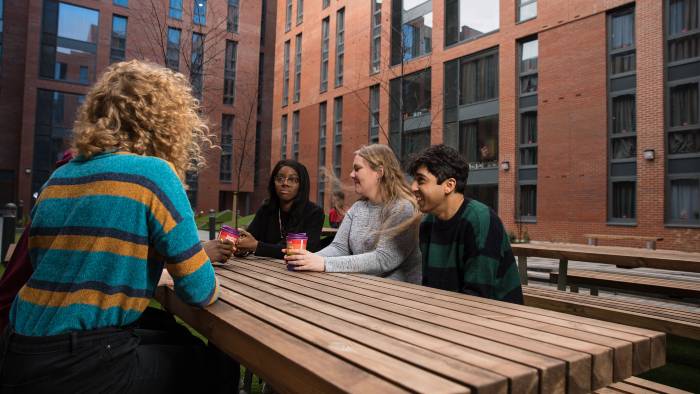 Group of students sat around a wooden table in a light open accommodation court yard.