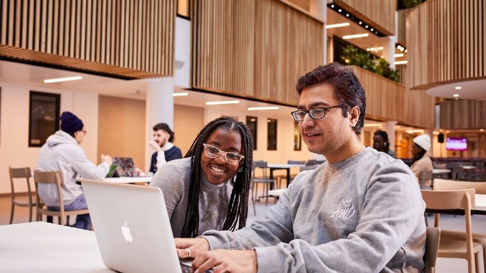 Two students sat using a laptop in the City Campus Atrium