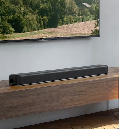 Wall-mounted TV screen in a living room showing a green mountain and field scene above a HT-X8500 soundbar as seen from the left