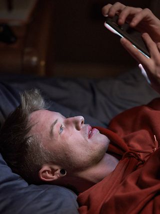 Young man lying on the bed and looking at his smartphone