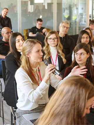 Sitting in a group of Femtec participants, one speaks into a microphone