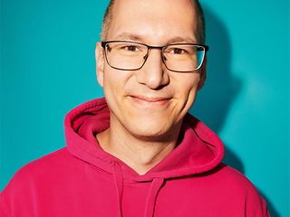 A man in a red hoodie looks into the camera with a friendly smile.