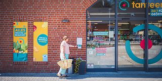 Woman with shopping bag opens supermarket door with access card.
