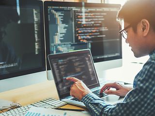 Male person sitting in front of a laptop on which code can be seen