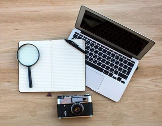 Overhead shot of laptop, notebook and camera on desk.