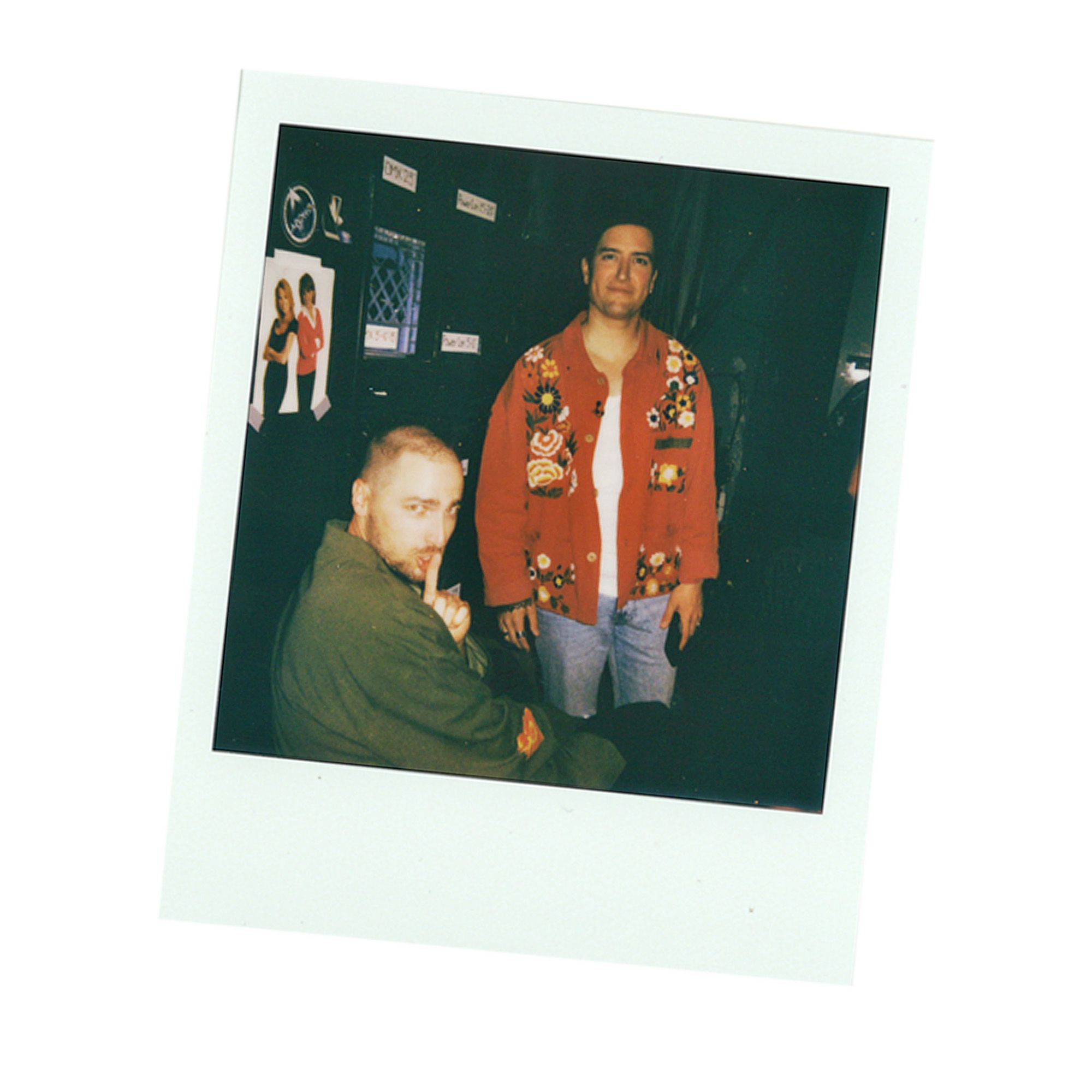 Polaroid of Kendall Schmidt making a 'shhh' hand motion, while Logan Henderson relaxes backstage before their performance for the Citi Concert Series on the TODAY show.