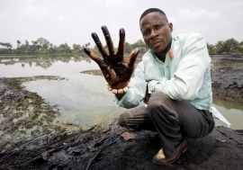 Claimant Eric Dooh shows the crude oil that has damaged the banks of the creek through his village in Ogoniland, Nigeria. 