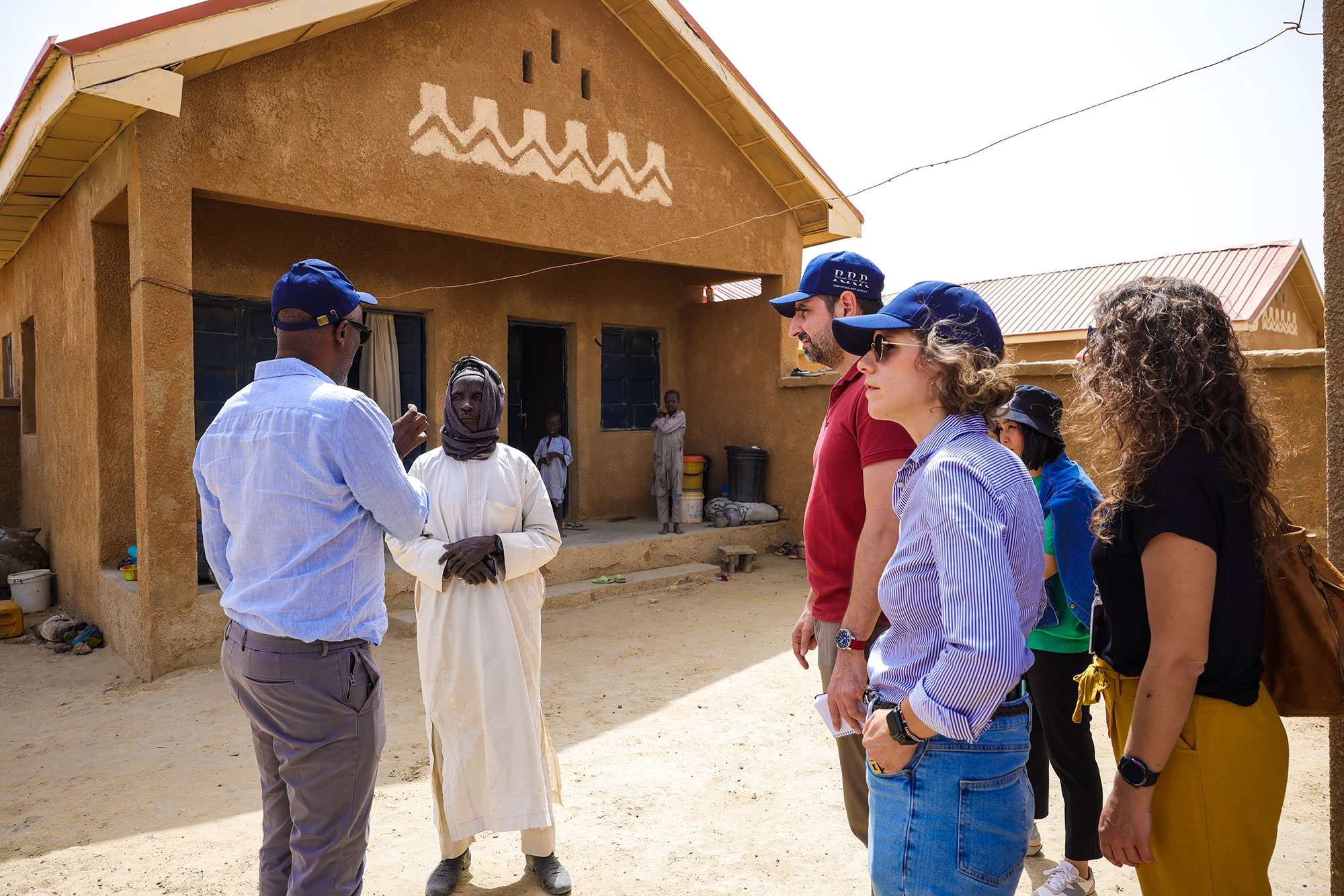 Mohamed Yahya is seen standing next to a beautifully decorated brown building as he talks with others surrounding him.