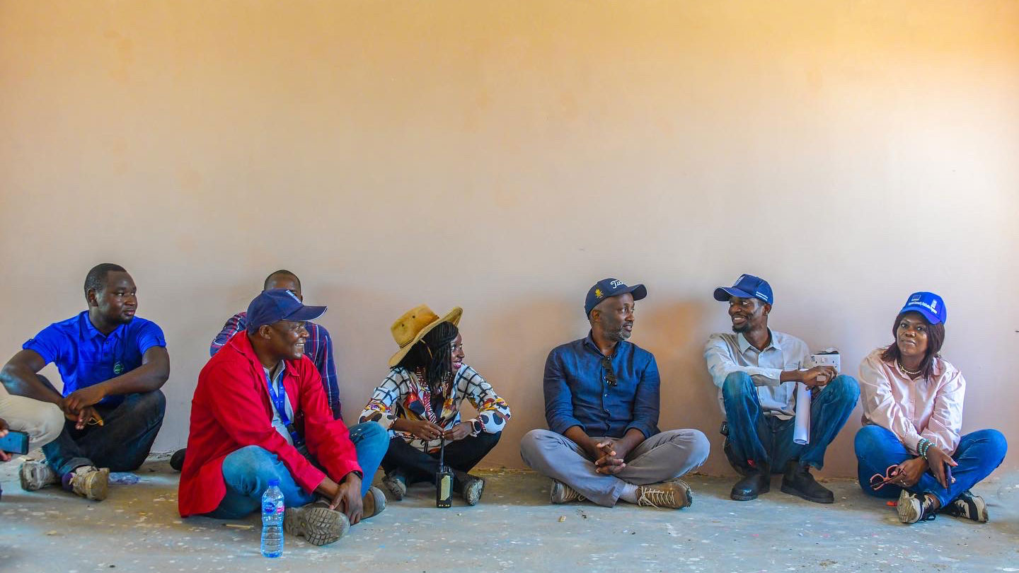 Mohamed Yahya and colleagues are seen sitting on the ground against a wall as they converse 