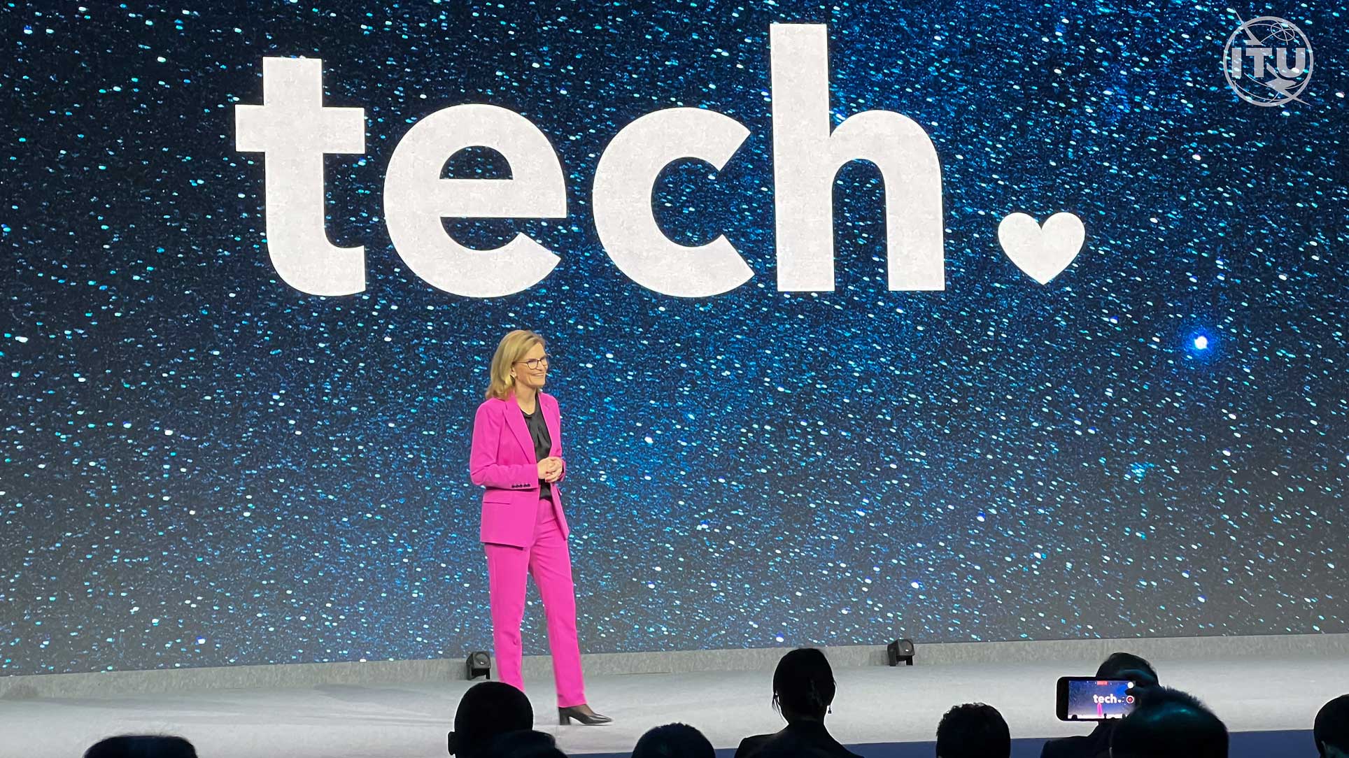 Doreen delivering a speech on platfrom and the word tech punctuated with a heart is seen in the background