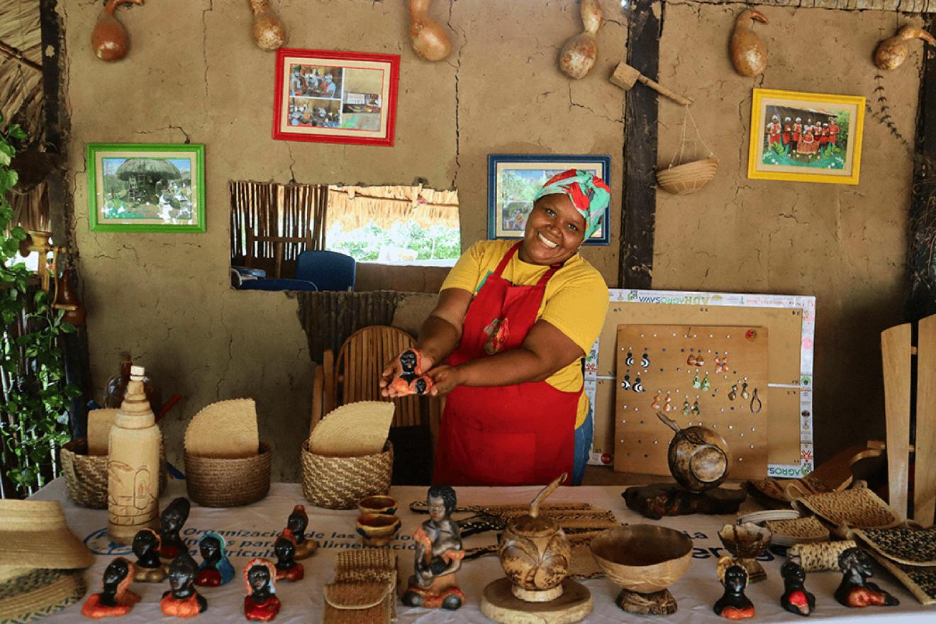 A smiling woman displays traditional handicrafts.