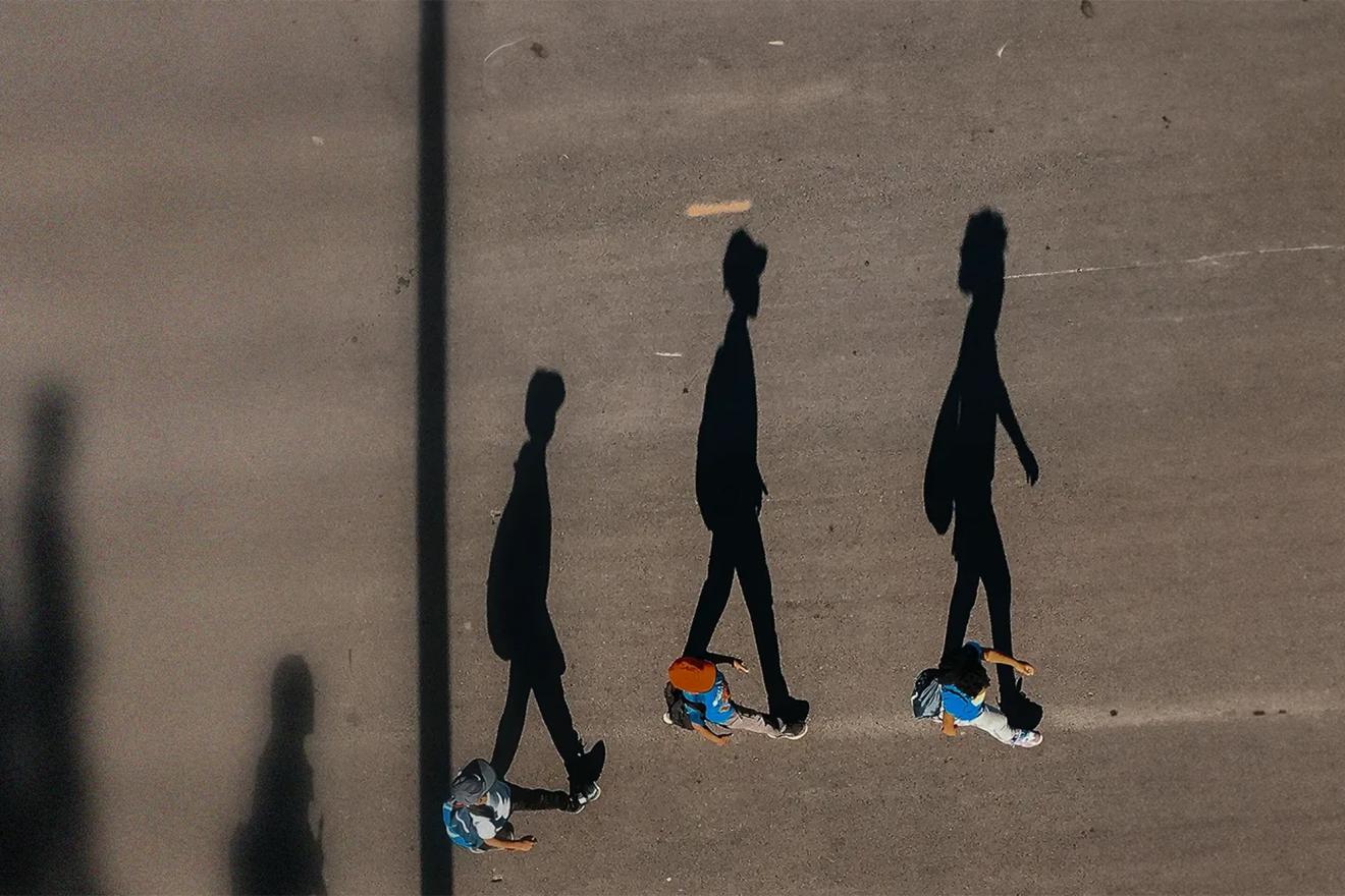 The shadow of three teenagers walking is cast on a road asphalt.