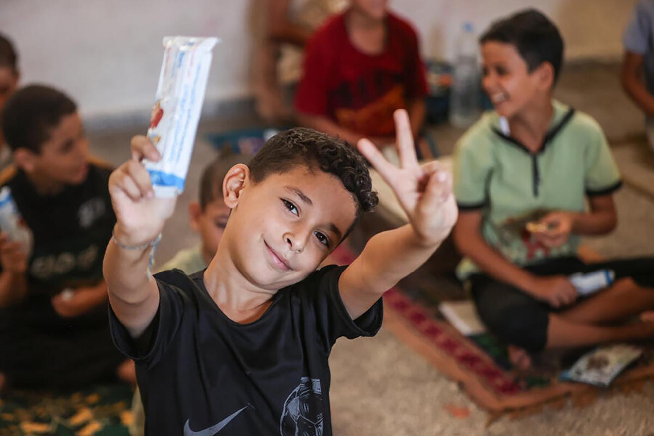 A child stands up and shows a date bar in a Gaza compound.