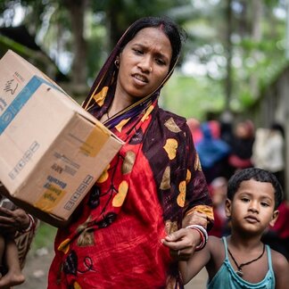 A flood-affected woman carrying the relief she received from WFP with her young son. Photo credit: WFP/Dip Chakma